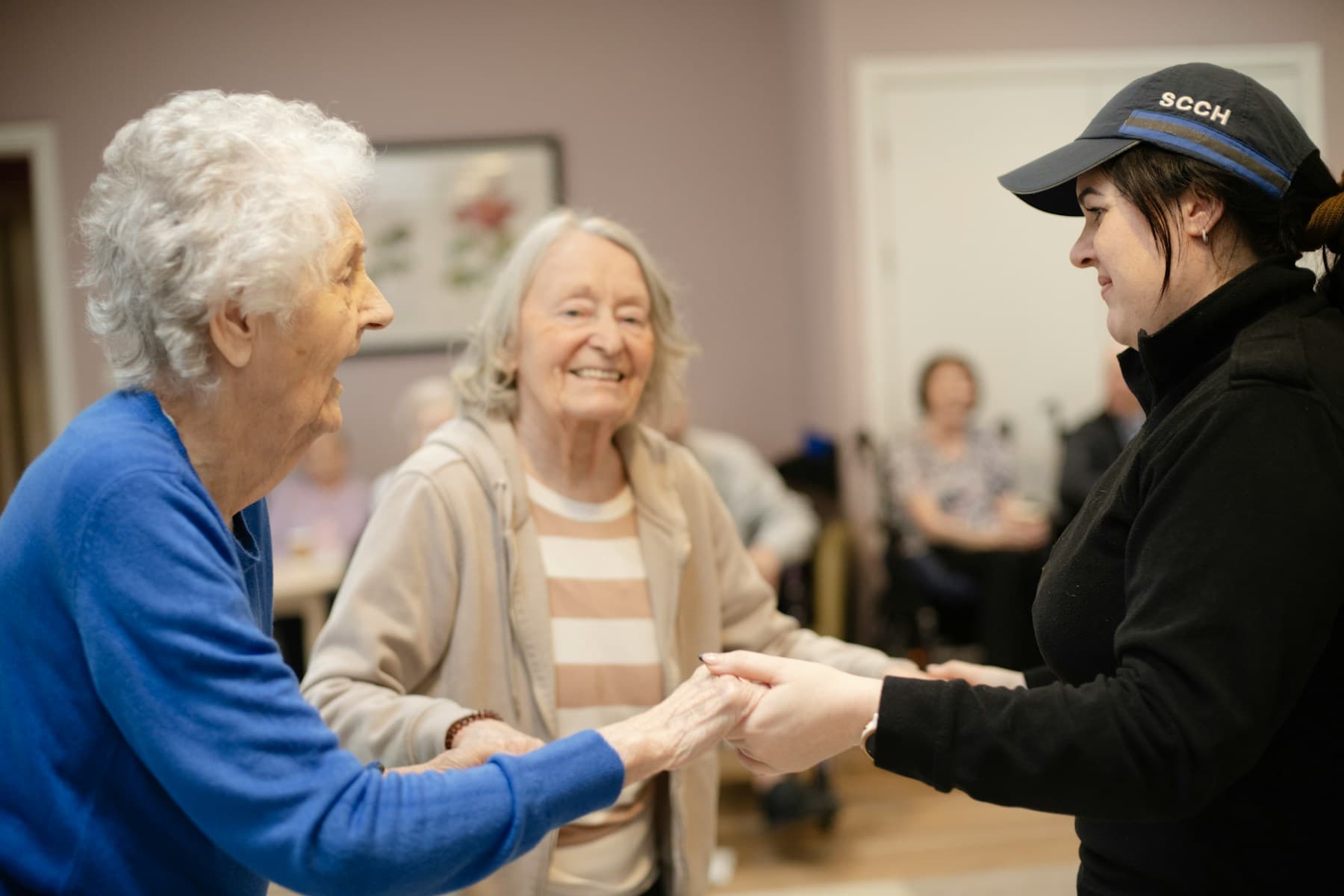 A younger woman holding hands with two older women during a visit