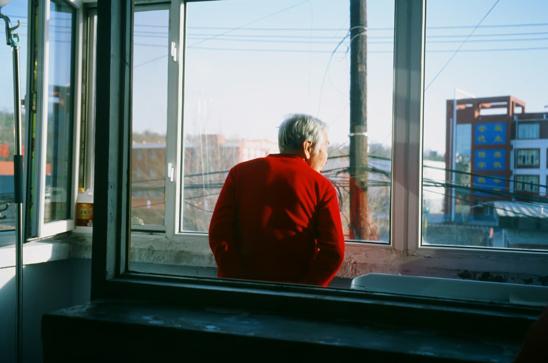 An older person in a red jumper looking out of a window