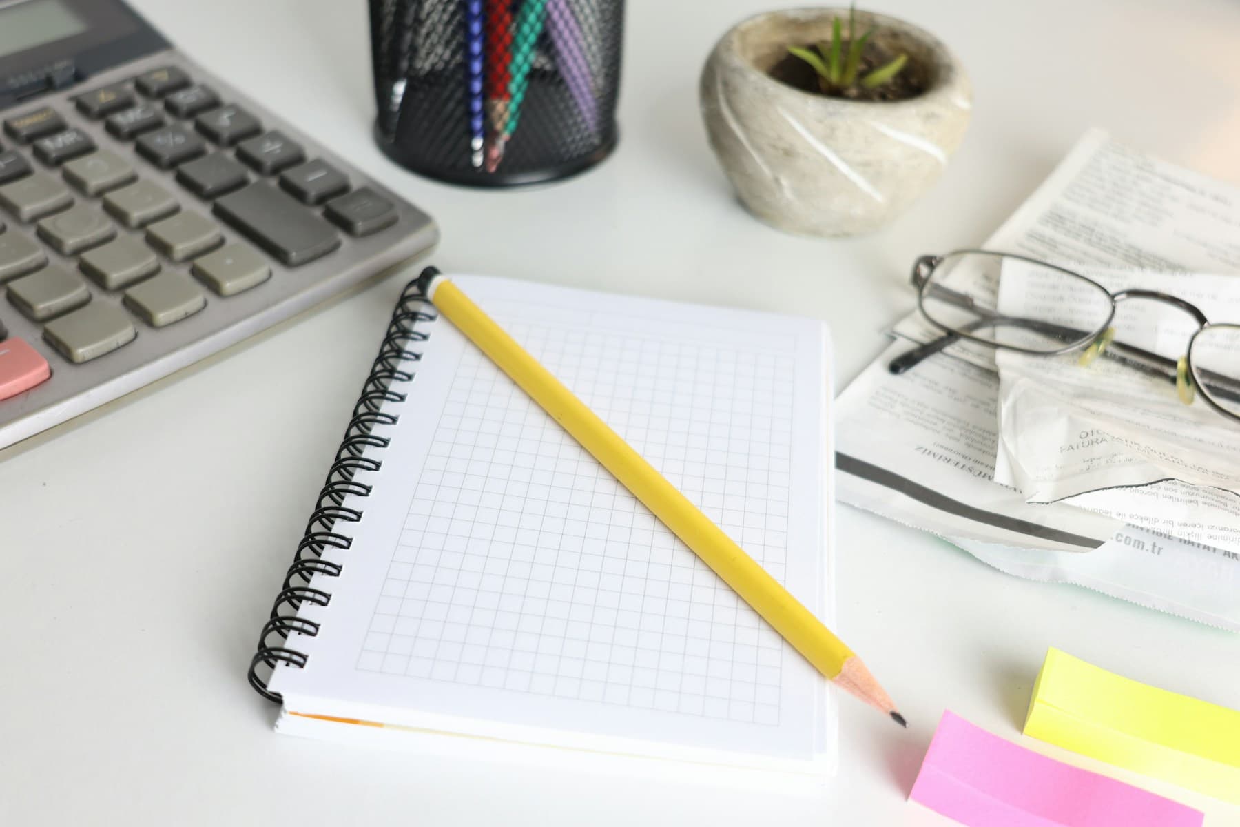 A desk with a calculator, notebook, pencil and glasses