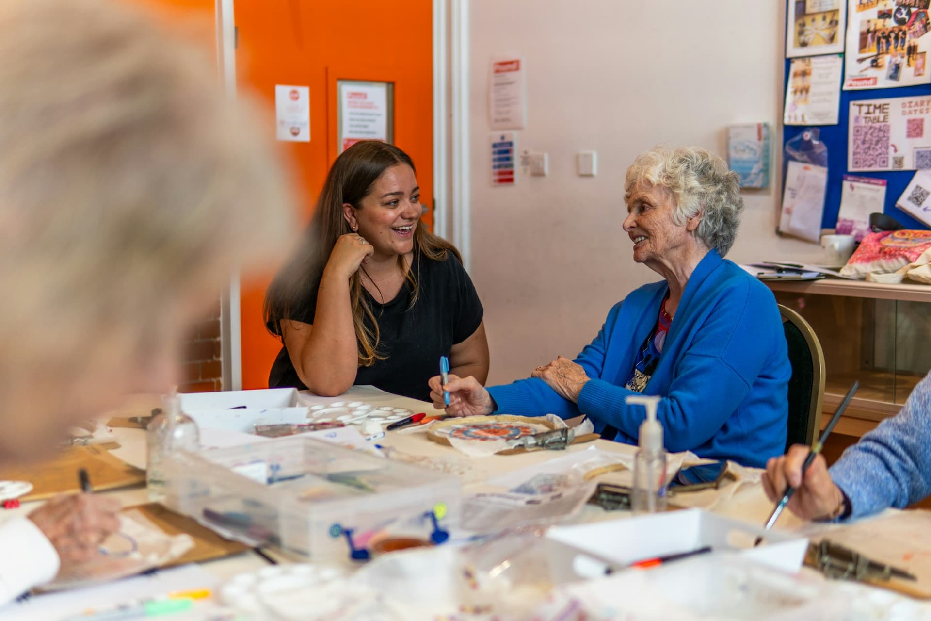A young woman and an older woman talking at a table during a community art class