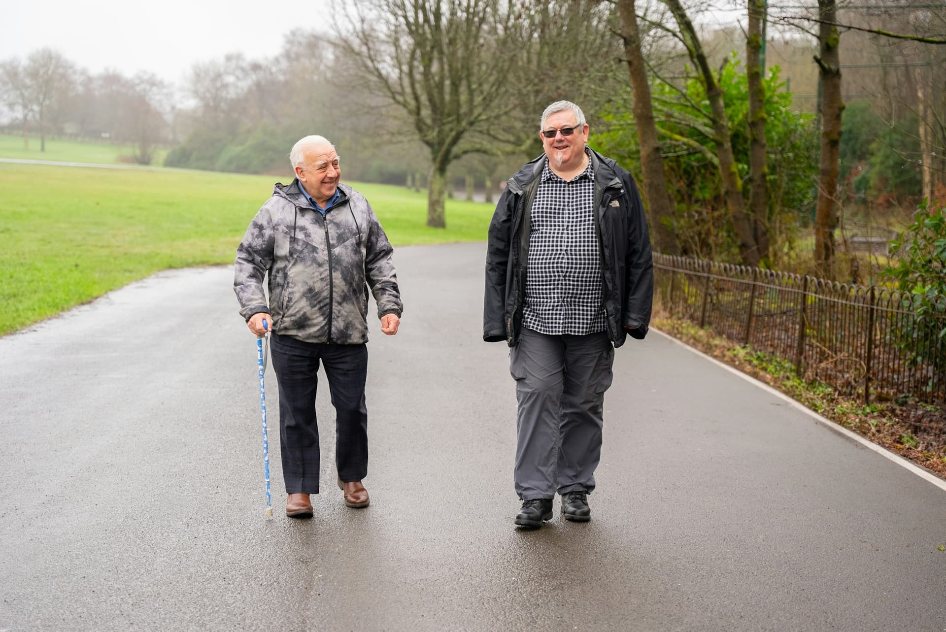 Two older men walking and chatting along a tree-lined park path