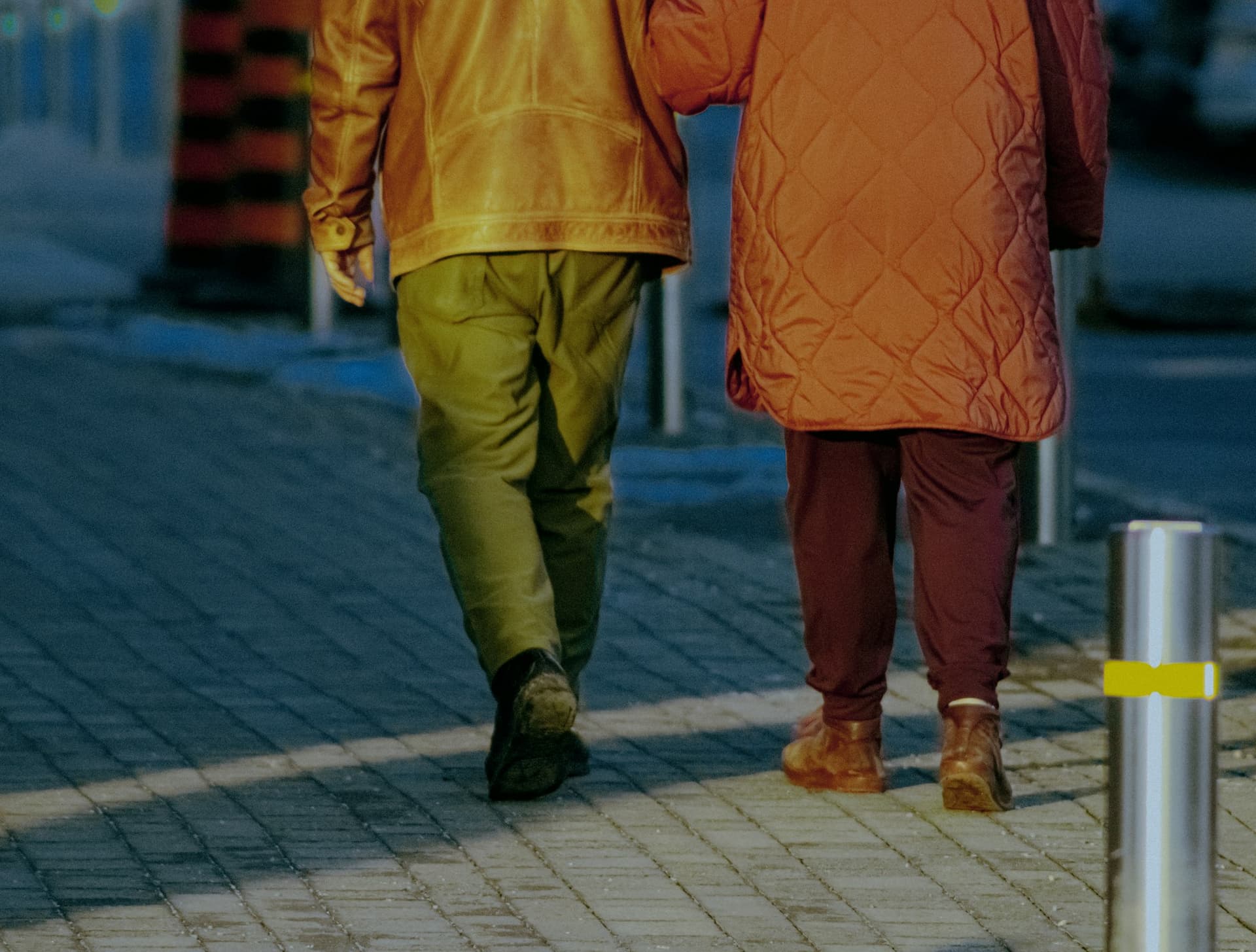 Two people walking arm in arm along a pavement